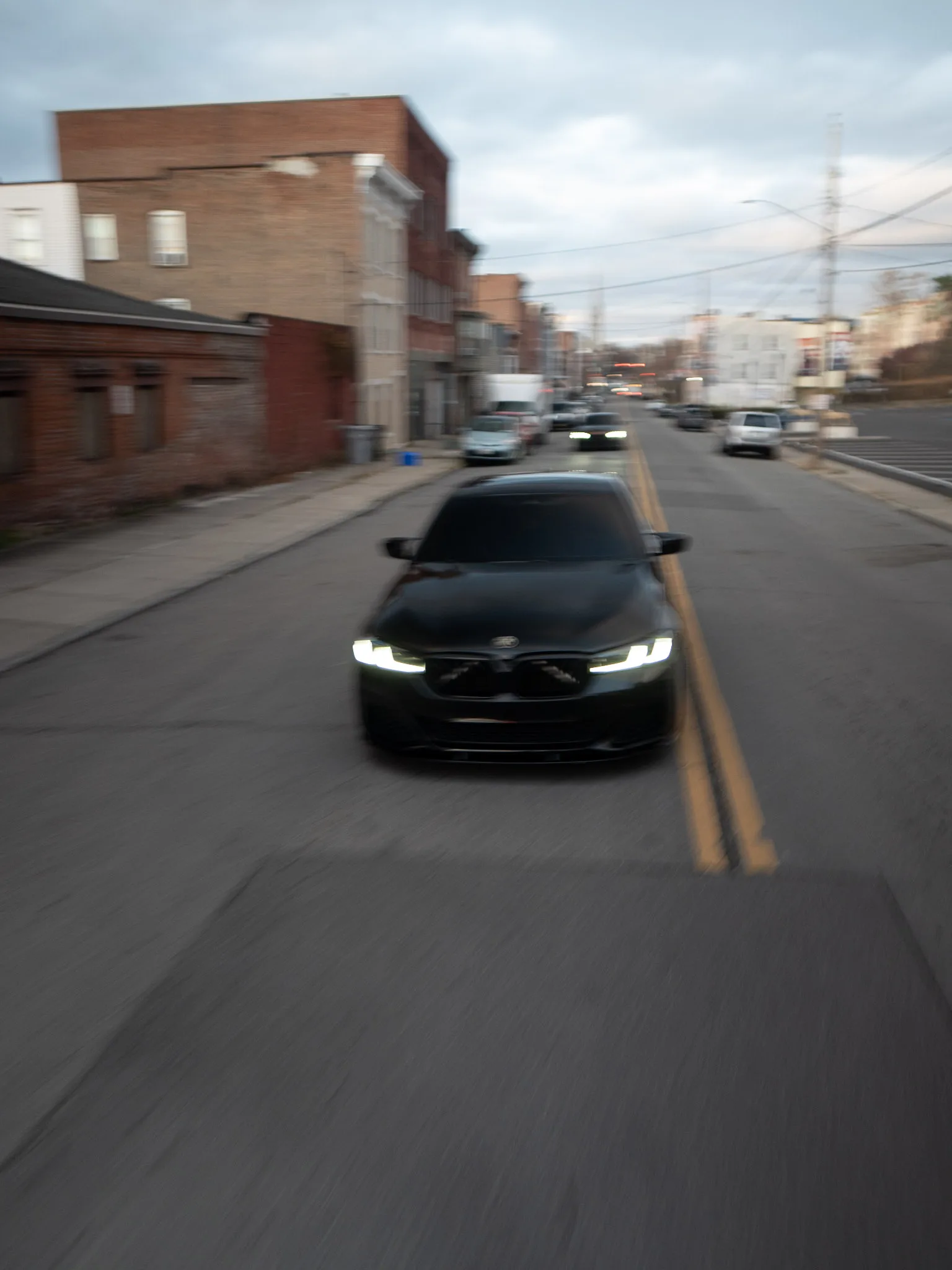 Black BMW sedan driving toward the camera down a brick-lined city street, heavy motion blur