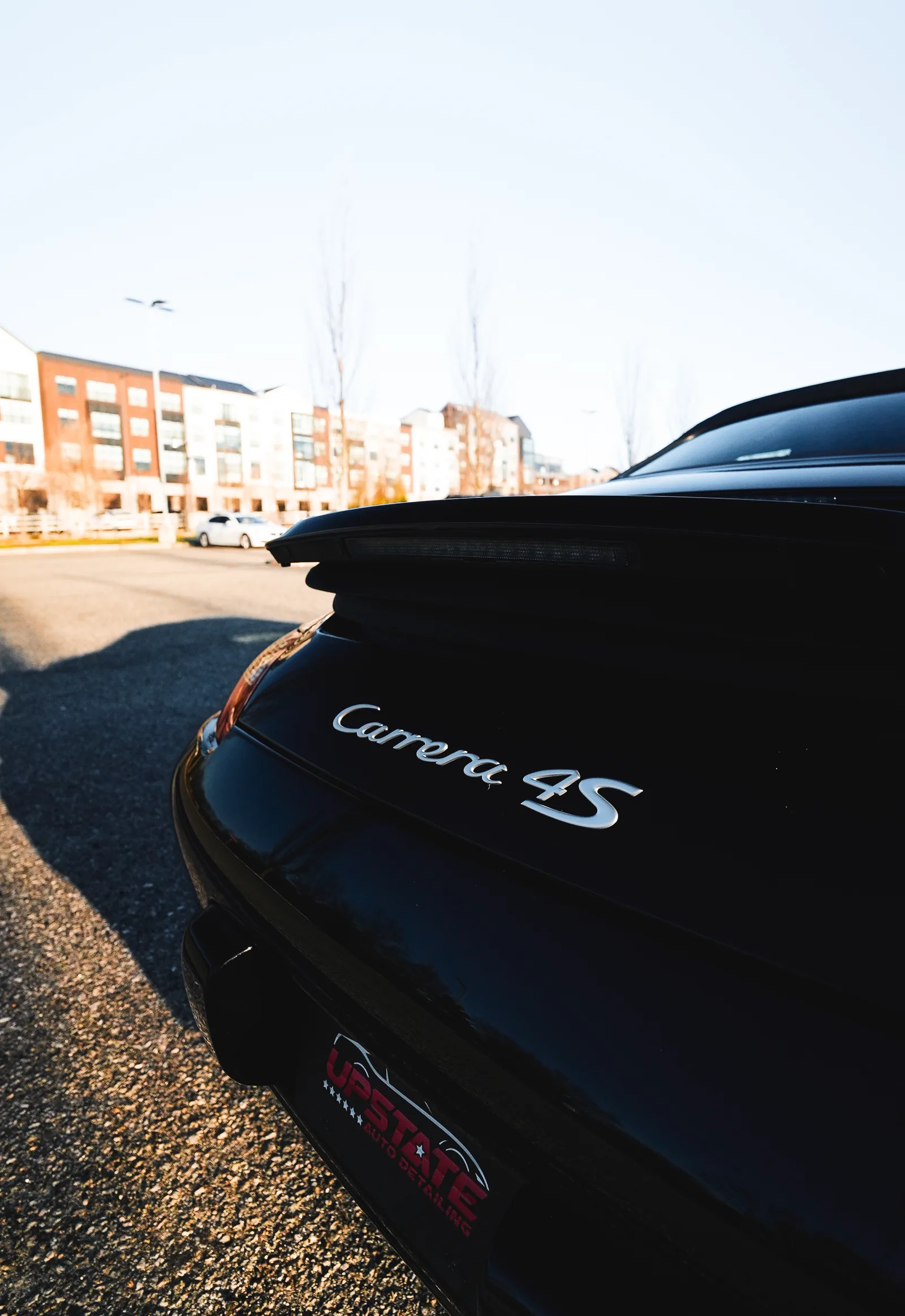Carrera 4S badge on the black rear deck of a Porsche above an Upstate plate insert, apartment buildings behind