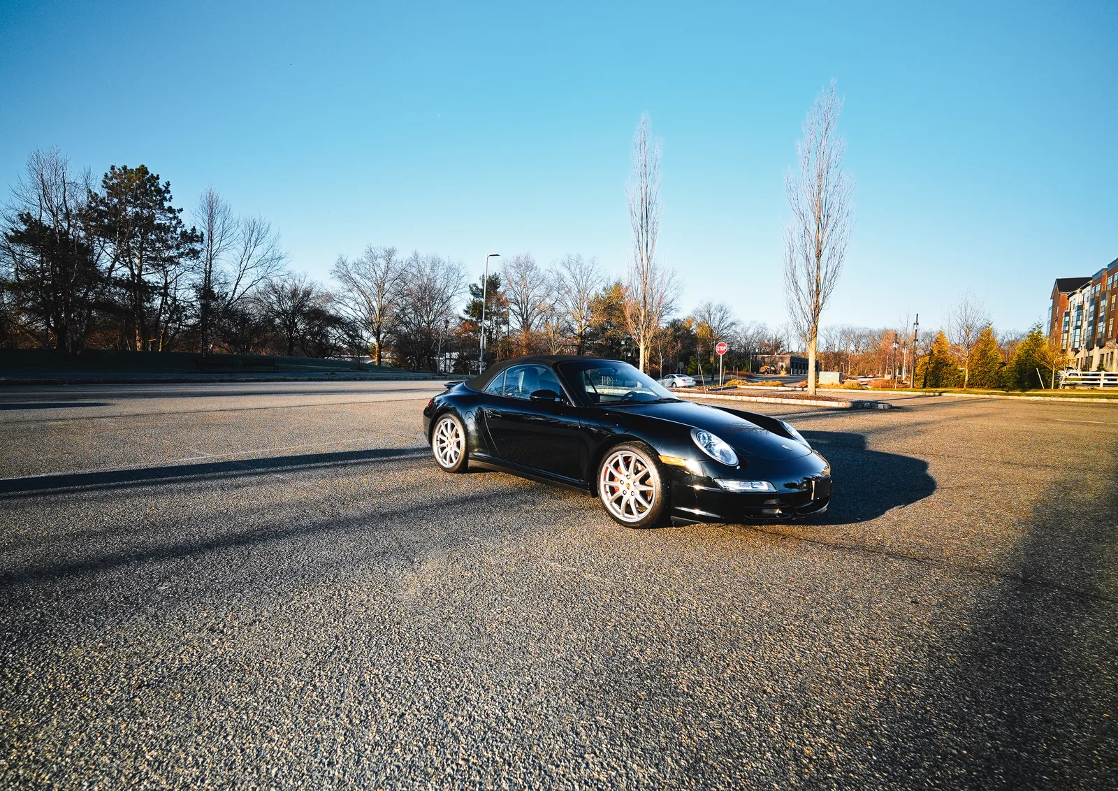Black Porsche convertible with the soft top up parked in a sunny empty lot, front three-quarter view