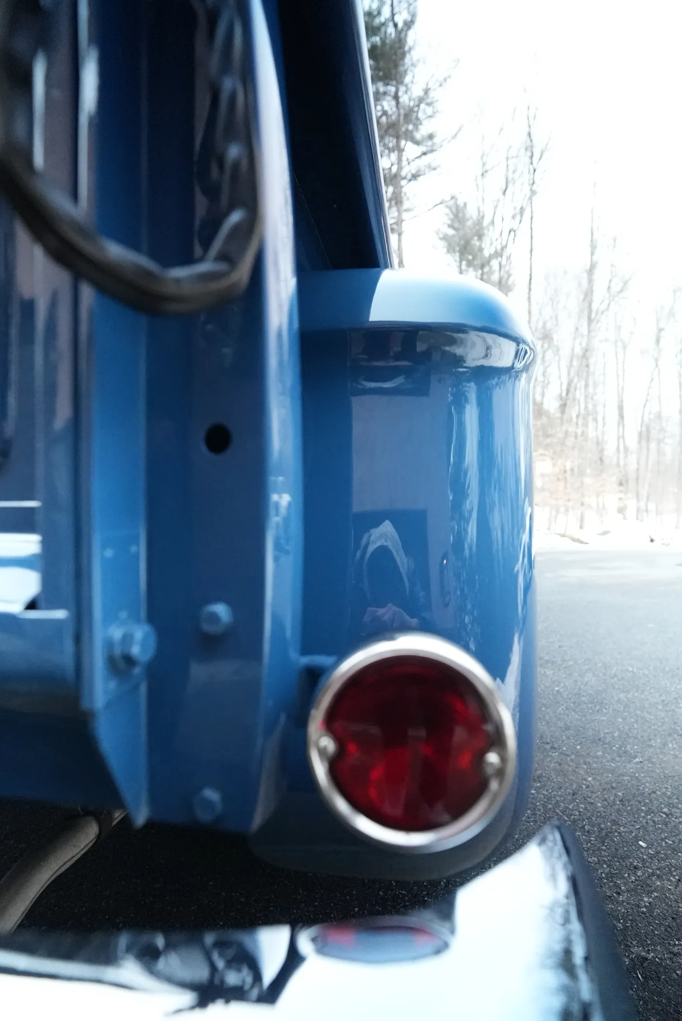 Round red tail light and rear fender of a blue classic pickup, with the tailgate chain above