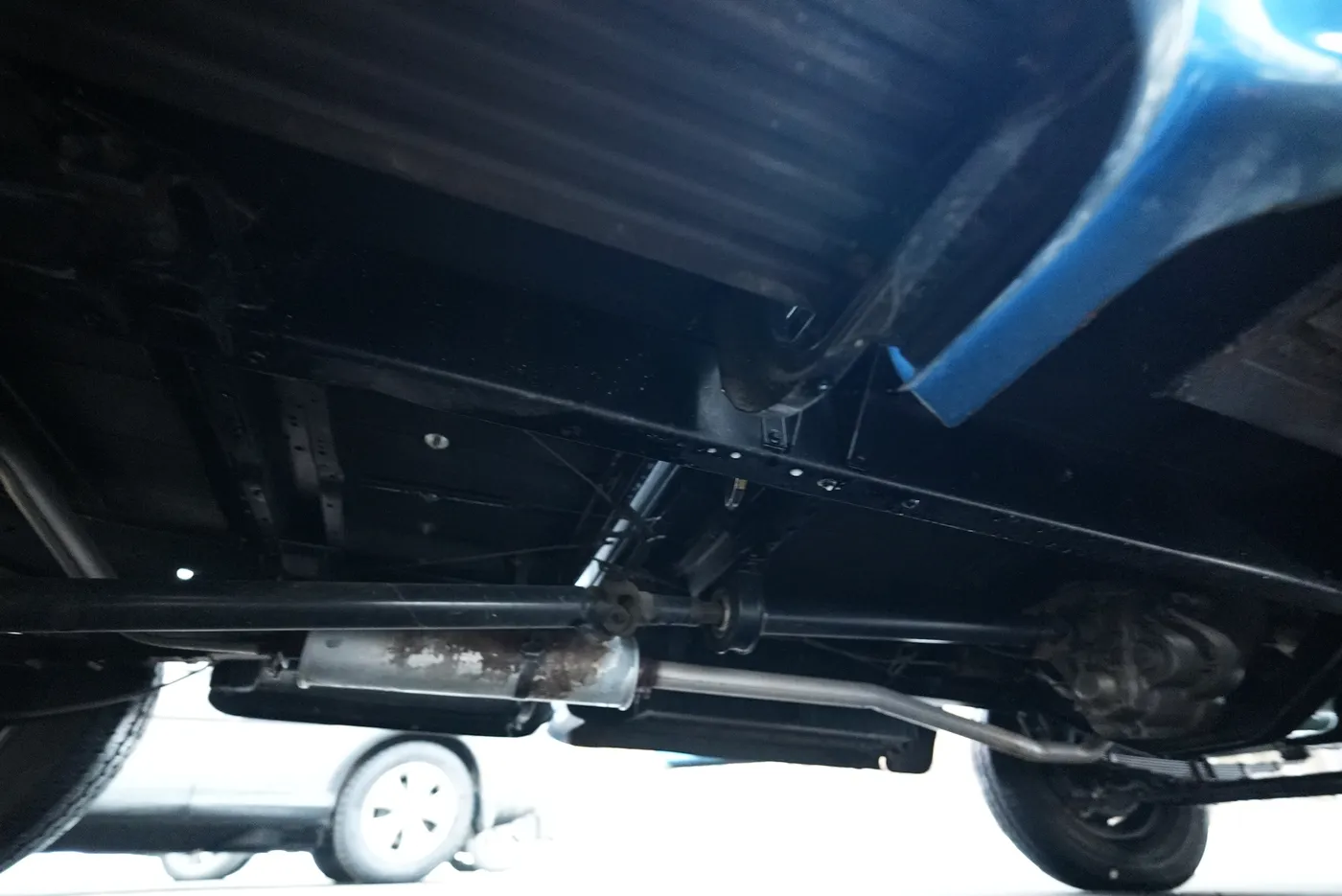 Low view of a vehicle underside showing the frame rail, exhaust pipe and muffler below a blue body panel
