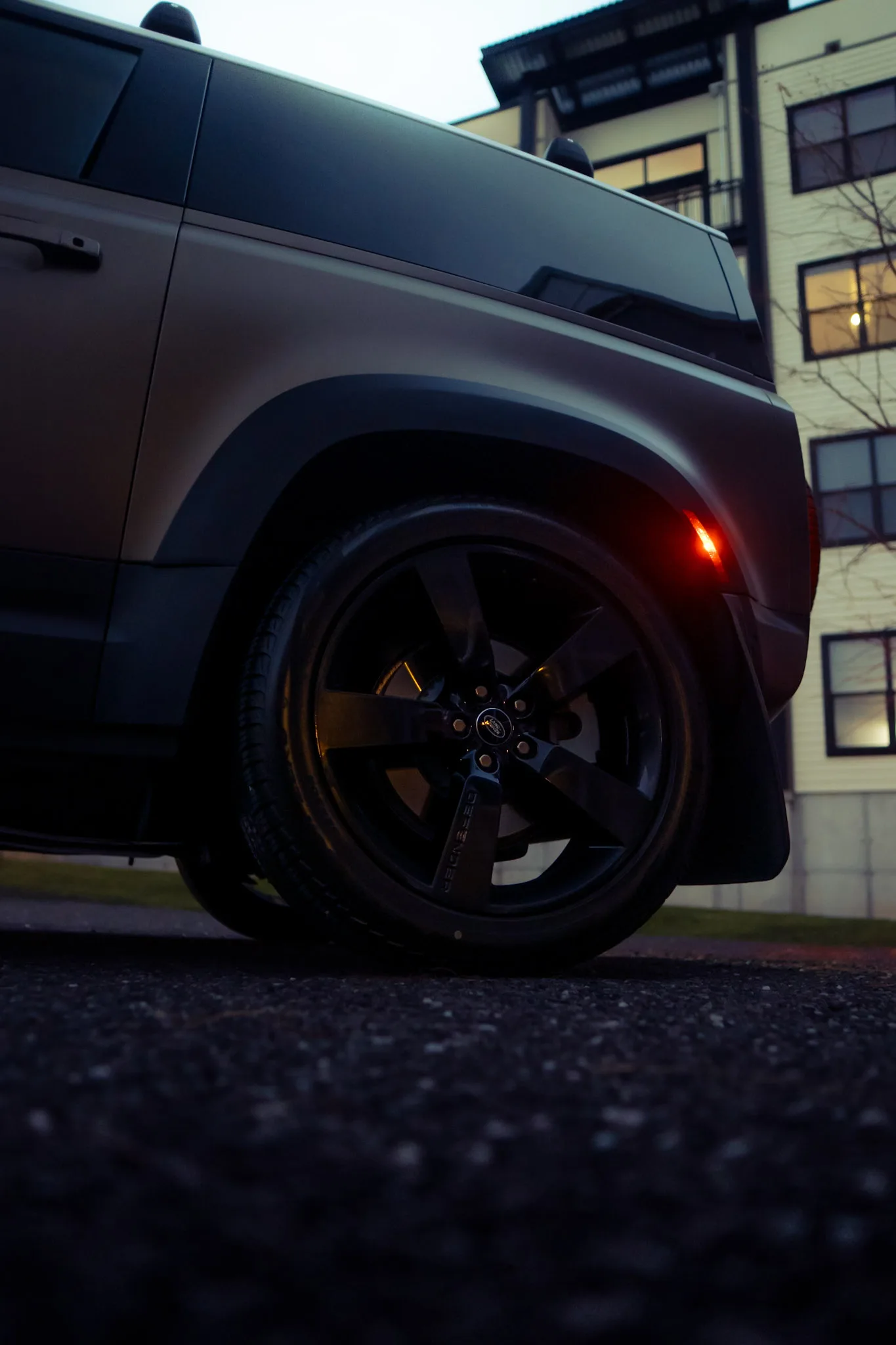 Low-angle view of a matte grey Land Rover Defender's black five-spoke wheel and wheel arch at dusk