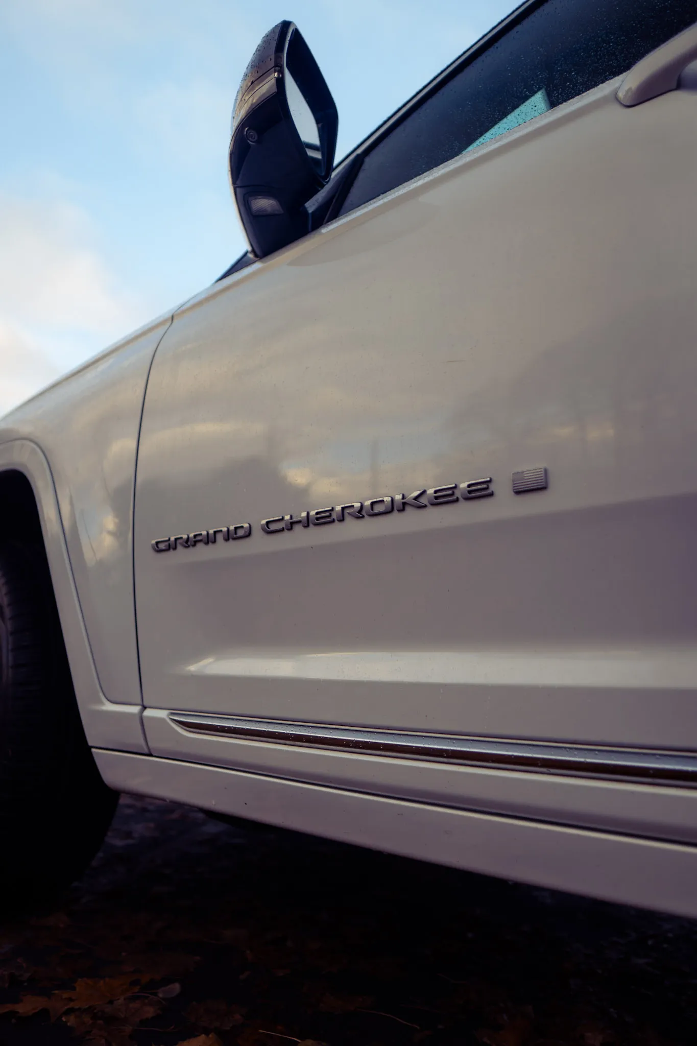 Upward view of the GRAND CHEROKEE door badge and side mirror on a white Jeep against blue sky
