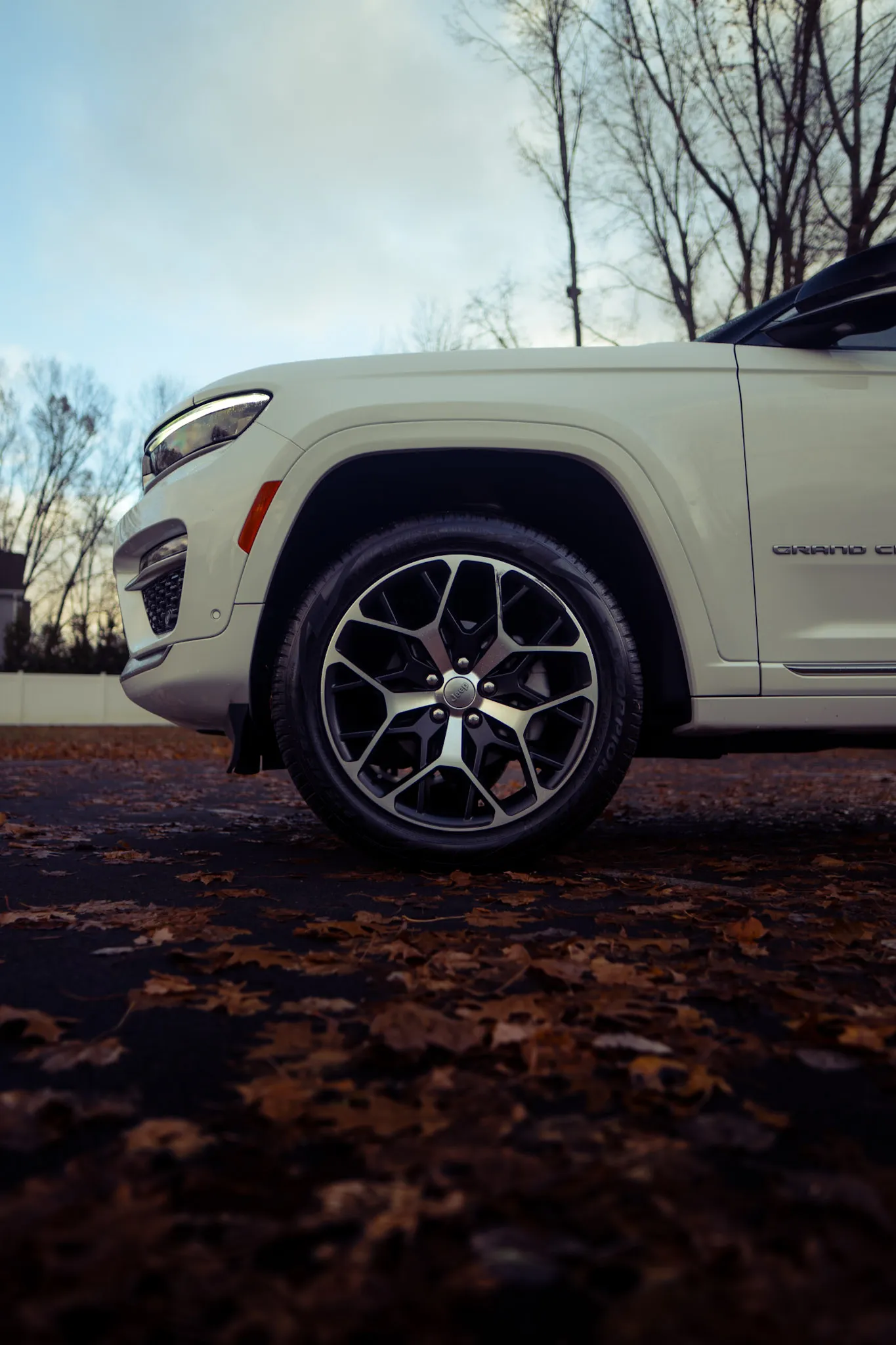 Low angle of the front wheel and fender on a white Jeep Grand Cherokee over fallen leaves