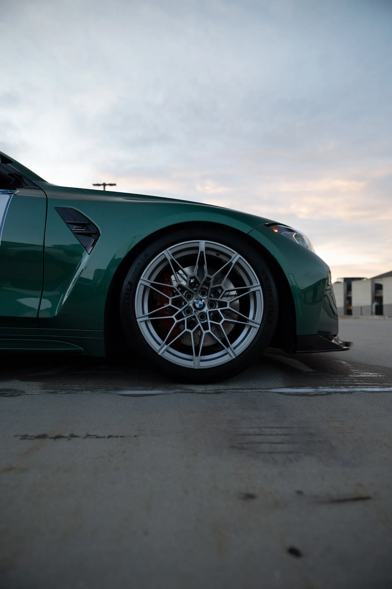 Side profile of a green BMW front fender, silver multi-spoke wheel and fender vent under an overcast sky