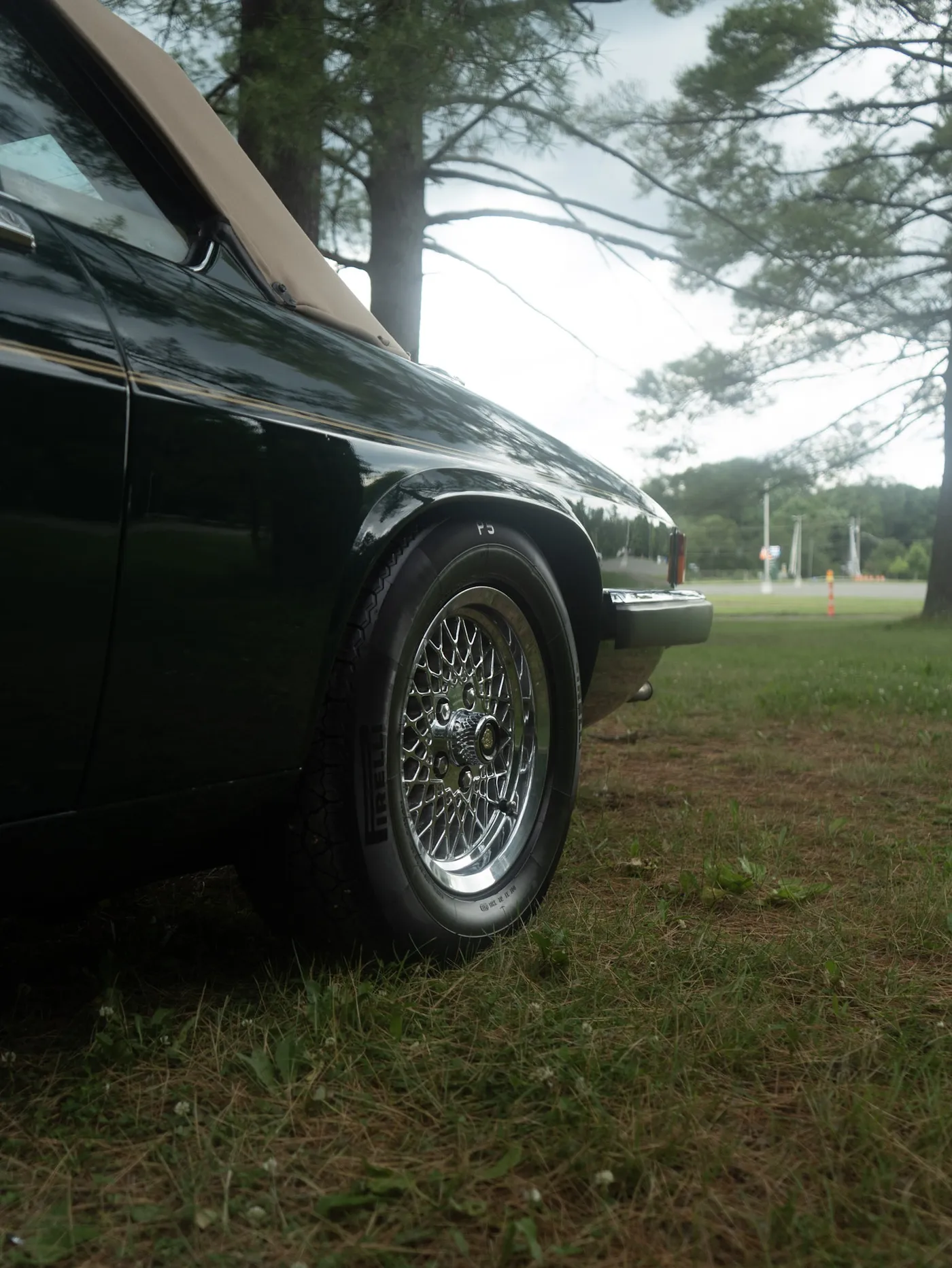 Front wheel and fender of a dark green Jaguar convertible with tan top parked on grass near a road