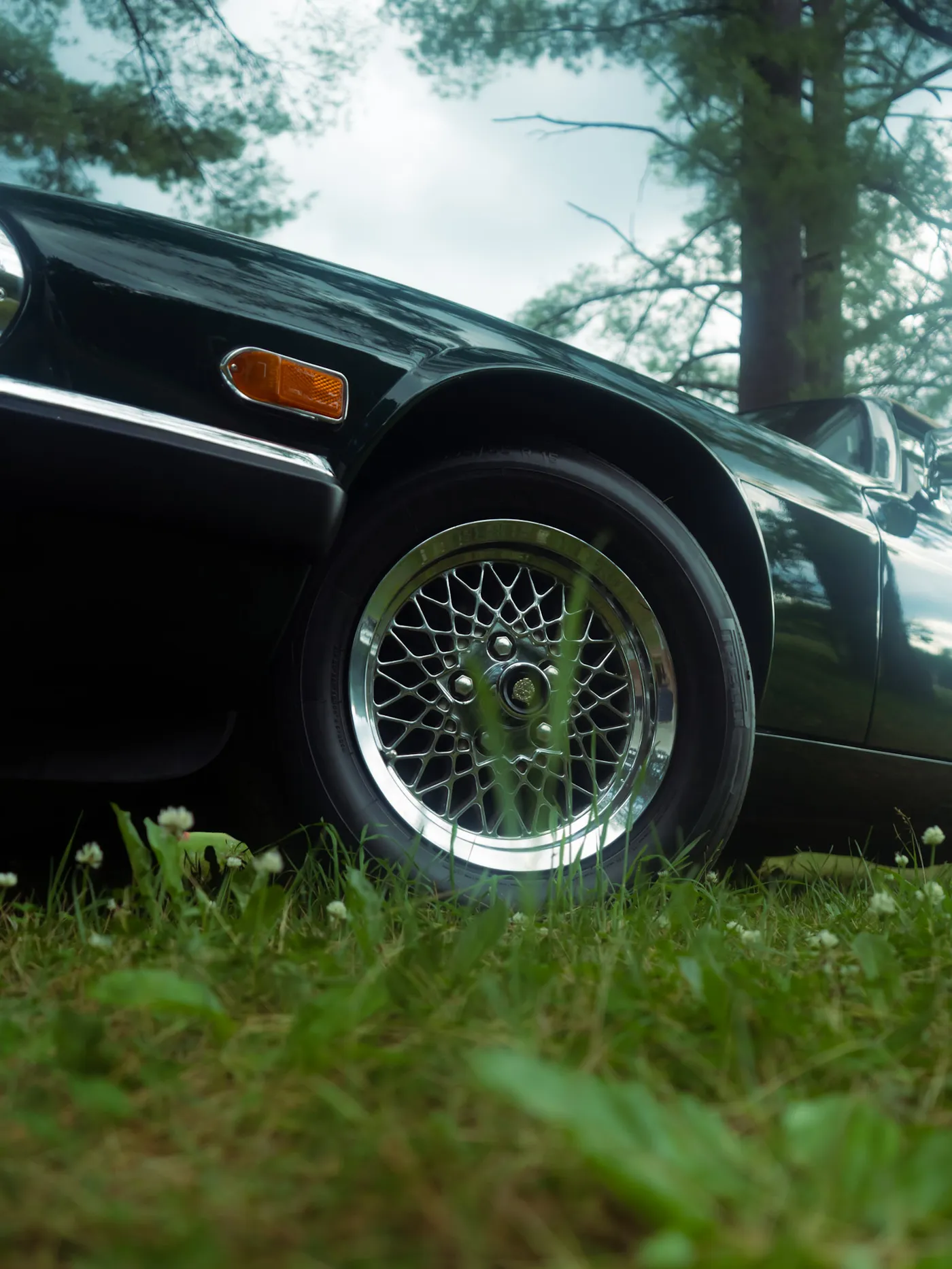 Low angle of a dark green Jaguar's lattice front wheel and orange marker with clover in front and cloudy sky