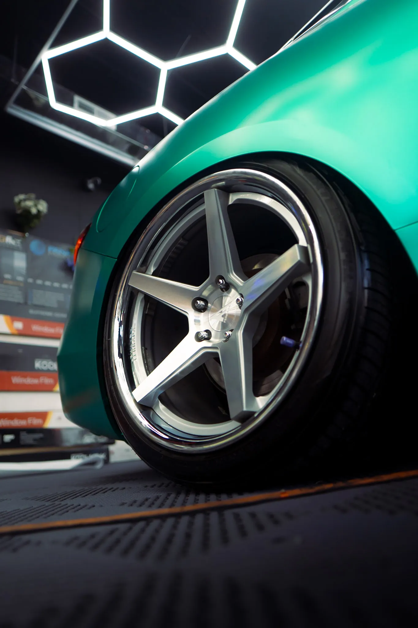 Rear five-spoke wheel with chrome lip on a matte teal car, window film boxes stacked in the background
