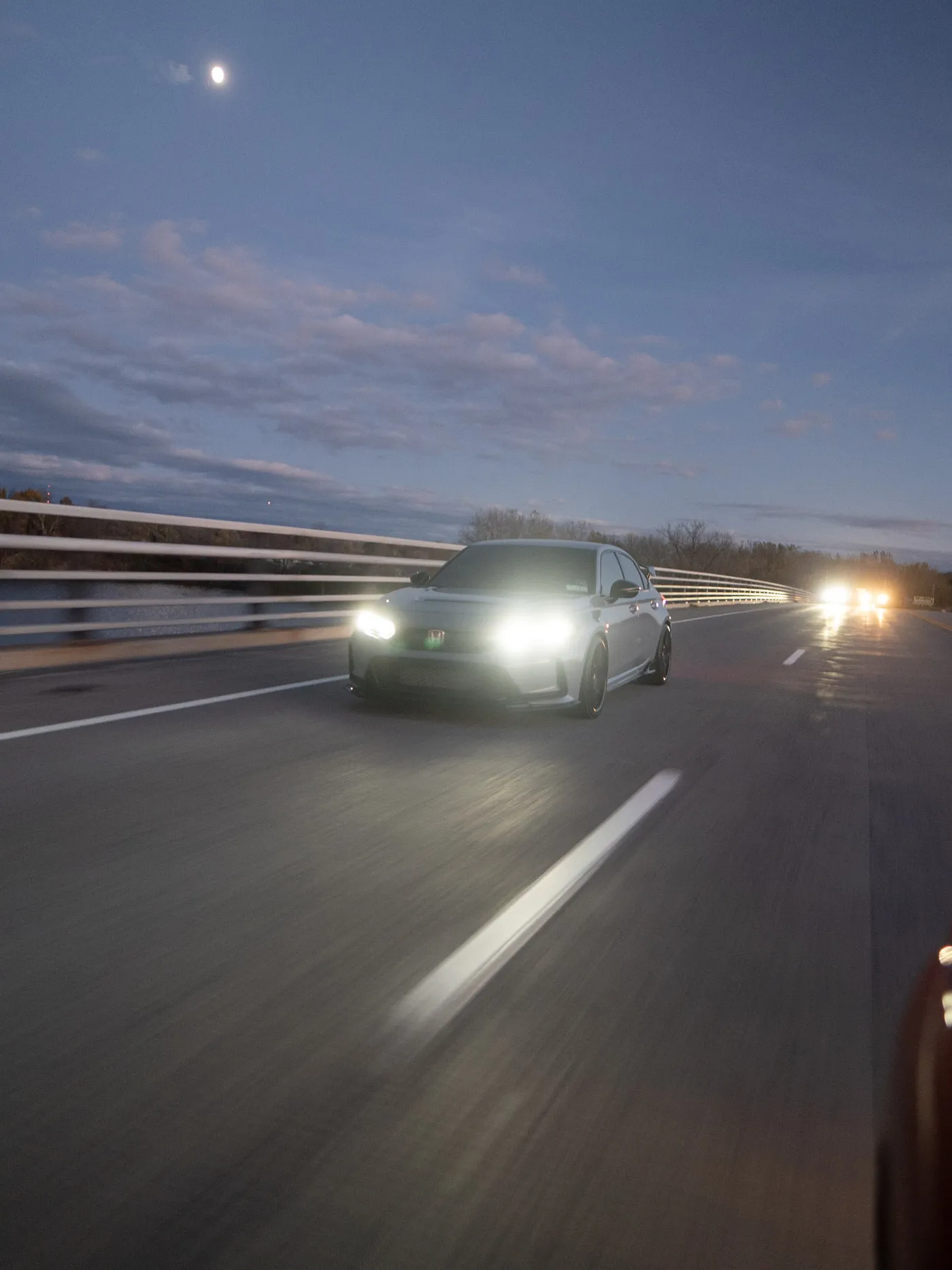 Gray Honda Civic Type R on a bridge under the moon, oncoming headlights glowing beyond the guardrail