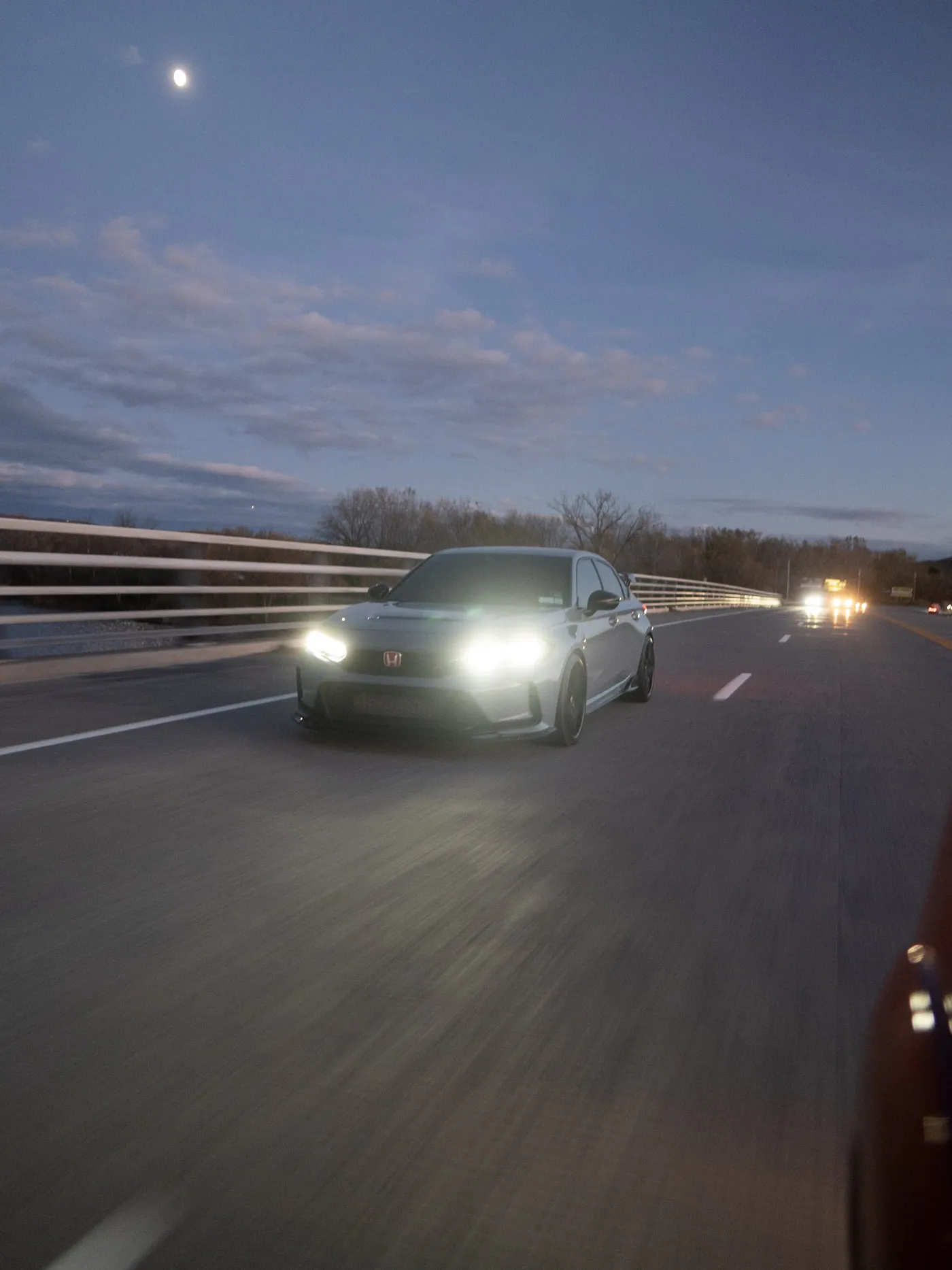 Gray Honda Civic Type R on a bridge at dusk, the moon high above and blurred open road in the foreground