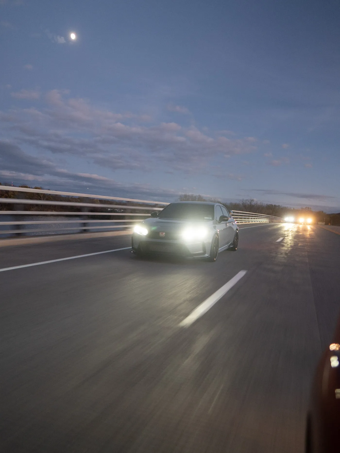 Gray Honda Civic Type R crossing a bridge under a rising moon, a lane stripe angled off its right side