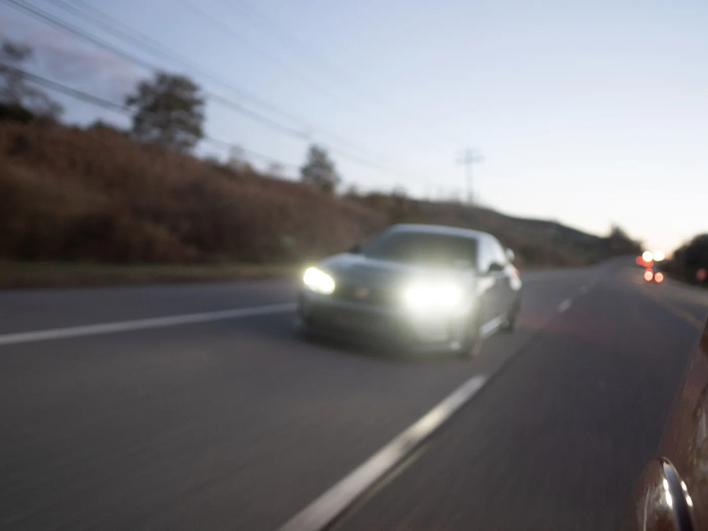 Soft-focus gray Honda Civic Type R approaching at dusk with bright headlights, a lane stripe at lower center