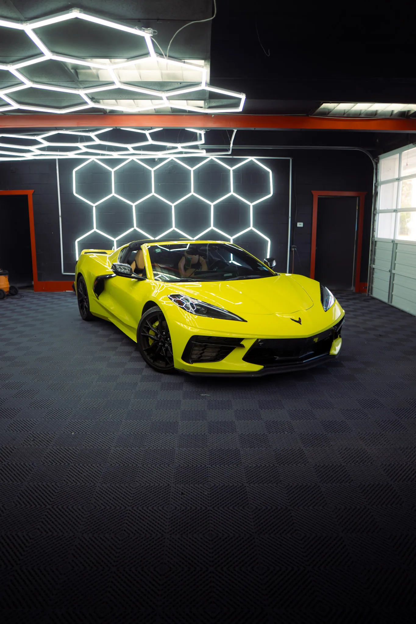 Yellow Chevrolet Corvette with its roof off parked under hexagon ceiling and wall lights indoors