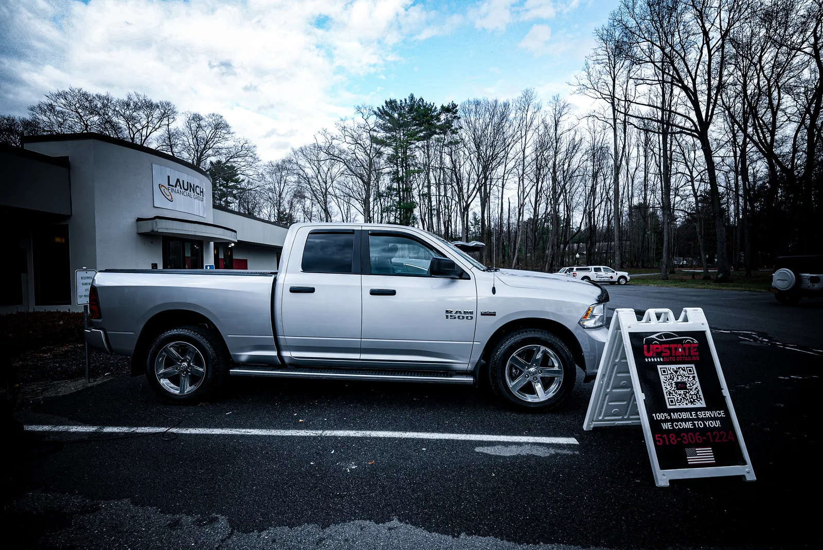 Silver Ram 1500 pickup parked beside an Upstate Auto Detailing mobile service A-frame sign in a parking lot