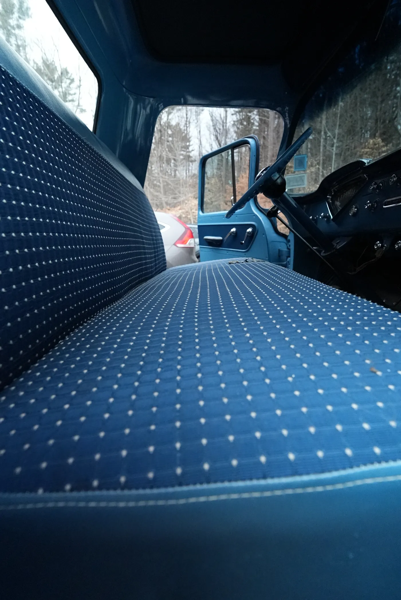 The blue patterned cloth bench seat inside a classic pickup truck, the driver door open behind it